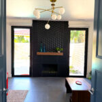 Modern fireplace with dark tile surround, wood mantel, and dual glass doors added for natural light and pool access in Sun Villas guest suite.