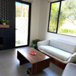 Midcentury-modern sitting area with textured sofa, walnut coffee table, matte black fireplace, and added windows for natural light in Sun Villas guest suite.