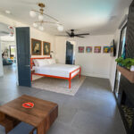 Guest suite with orange metal bed frame, black tile fireplace, dusty blue doors, and midcentury pop art decor — part of a multigenerational remodel in Sun Villas, Palm Springs.