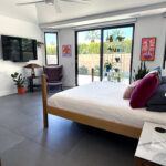 Primary bedroom in Sun Villas remodel featuring large format tile flooring, modern wood bed, sliding glass doors, accent art, and indoor-outdoor views.