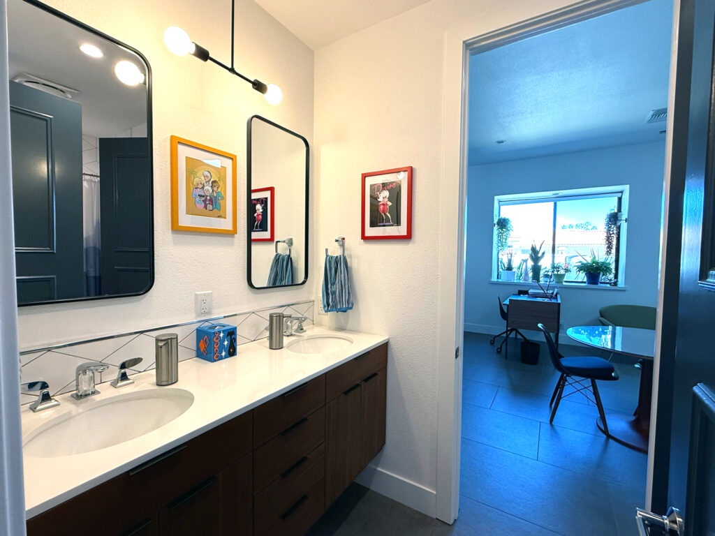 Double vanity bathroom remodel with new lighting, mirrors, tile backsplash, updated faucets, and modern walnut cabinetry in Sun Villas project.