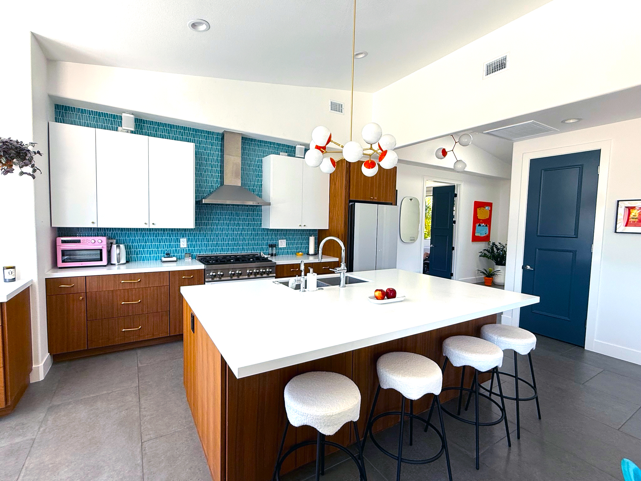 Sun Villas kitchen – Palm Springs home renovation. Midcentury-inspired kitchen remodel with custom walnut cabinetry, blue geometric tile backsplash, large white island with barstools, and reconfigured open floor plan.